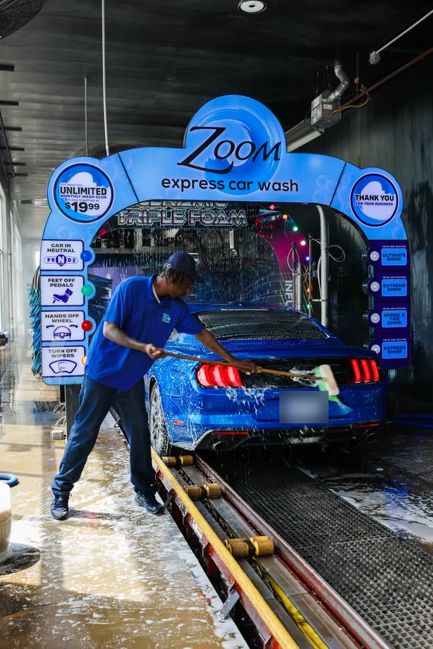 An attendant scrubbing a blue car as it rolls under the Zoom Express arch
